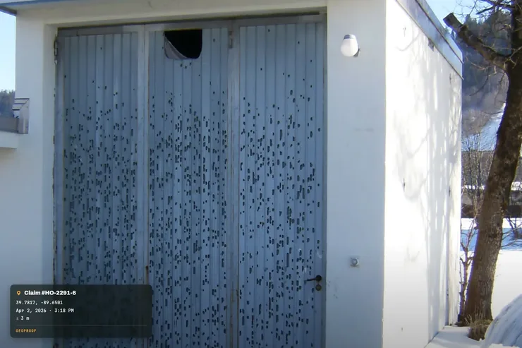 A real photo of hail-impact dents pockmarking a metal garage door, with GPS coordinates, a claim number and timestamp added into the bottom-left corner as an example of GeoProof's stamp